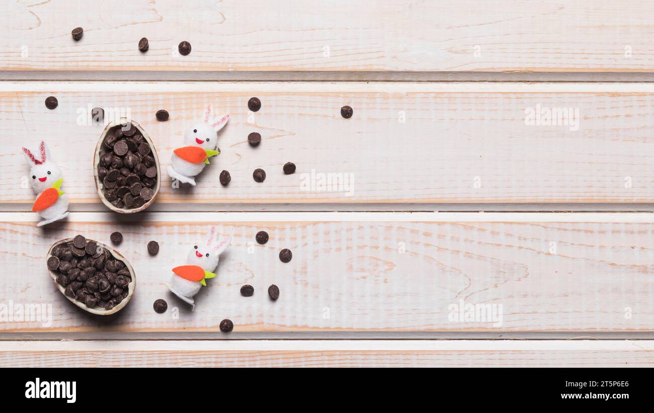 Tre coniglietti bianchi con uovo di pasqua rotto ripieni di choco chips da scrivania in legno Foto Stock