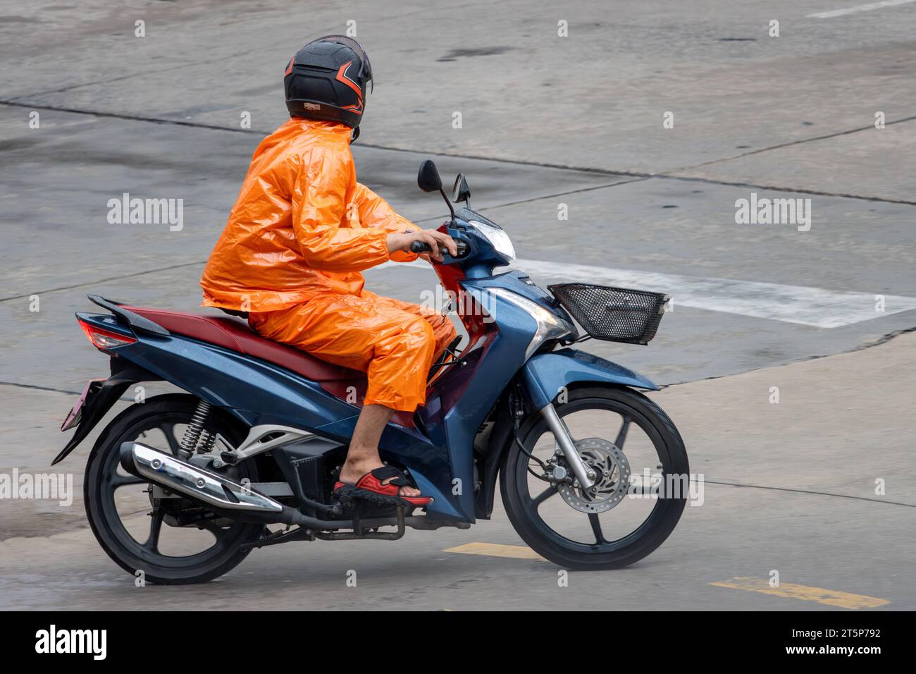 Un uomo con un impermeabile cavalca una moto sulla strada bagnata, Thailandia. Foto Stock