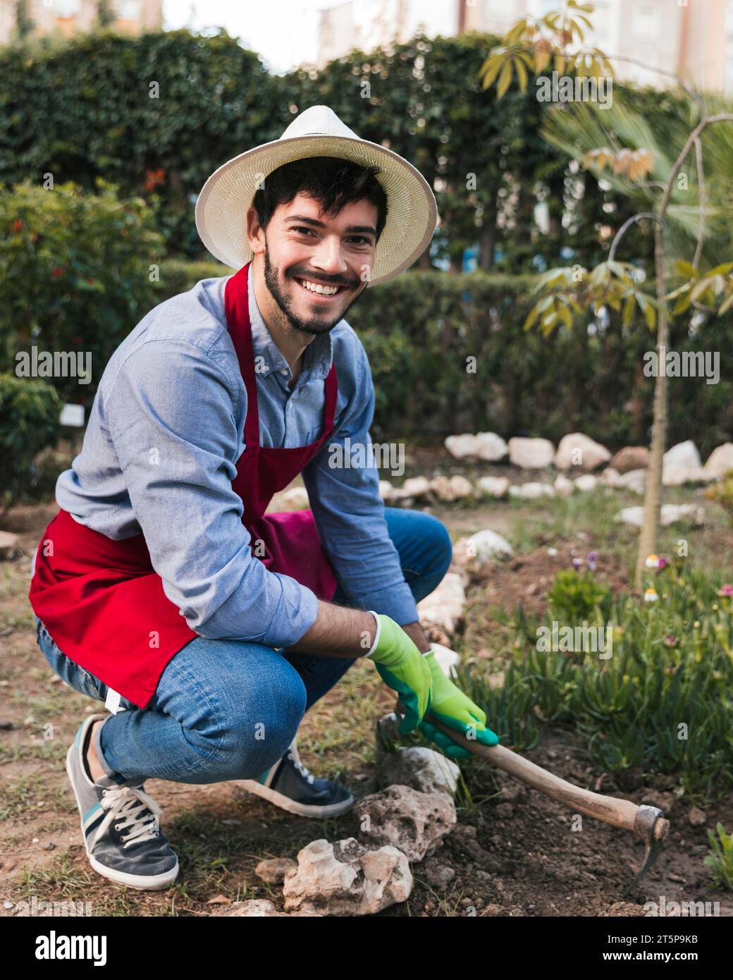 Ritratto sorridente giardiniere maschio che scava terreno con l'orto della zappa Foto Stock