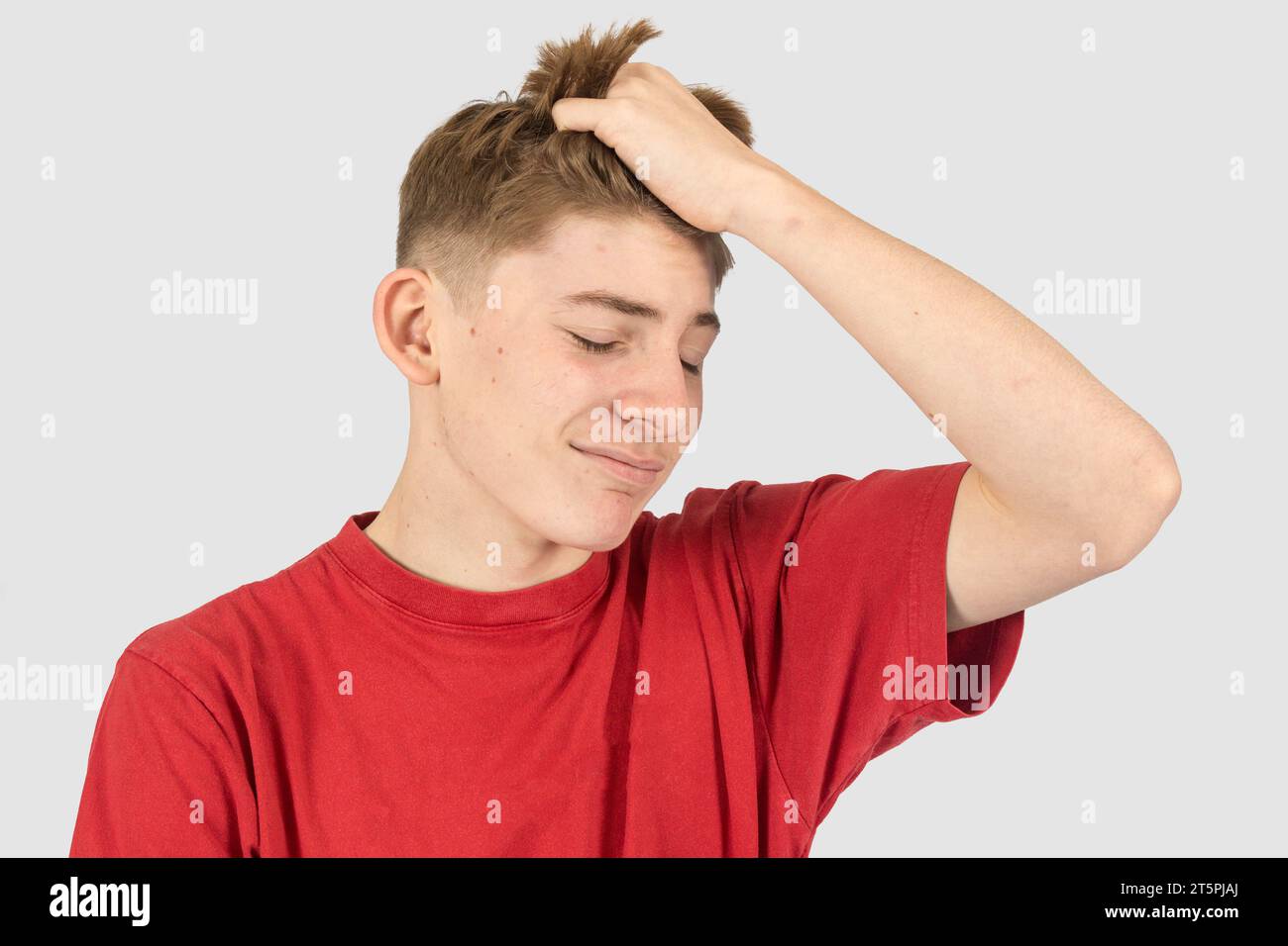 Un ritratto in studio di un adolescente infastidito di quindici anni, che gli corre le mani tra i capelli Foto Stock
