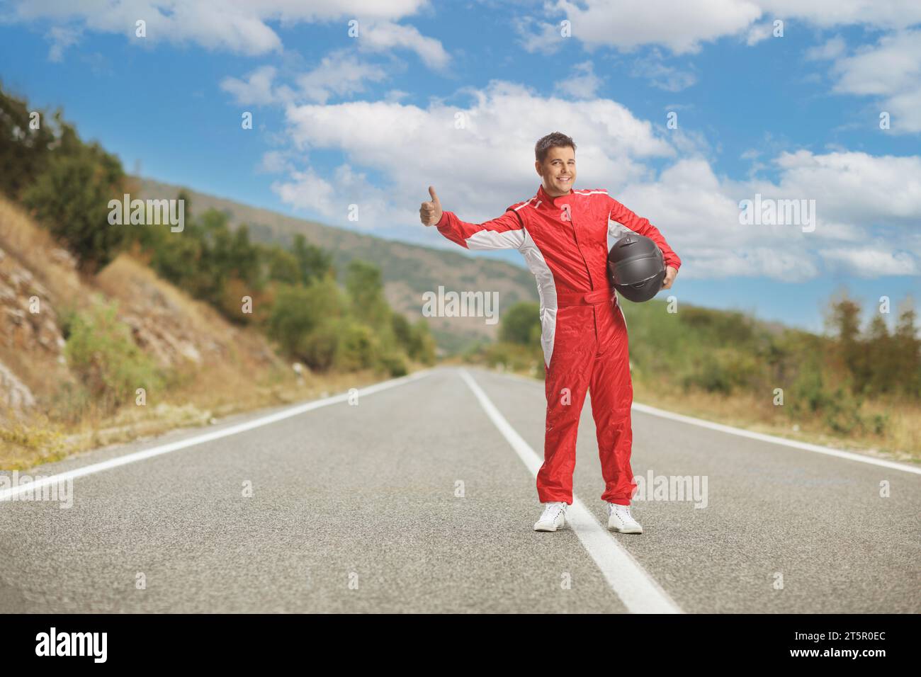 Scatto completo di un pilota in costume rosso con un casco e un autostop su una strada aperta Foto Stock