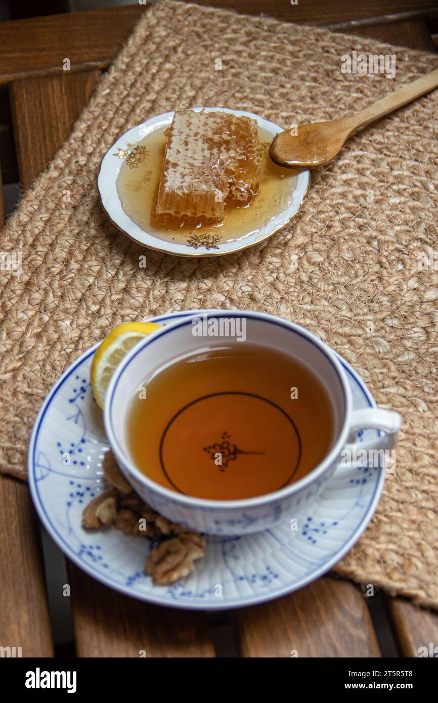 Disposizione mattutina su un tavolo di legno sul balcone, libri da leggere, tazza di tè naturale, teiera, miele biologico della fattoria, foglie di tè verde fresco e frutta biologica Foto Stock