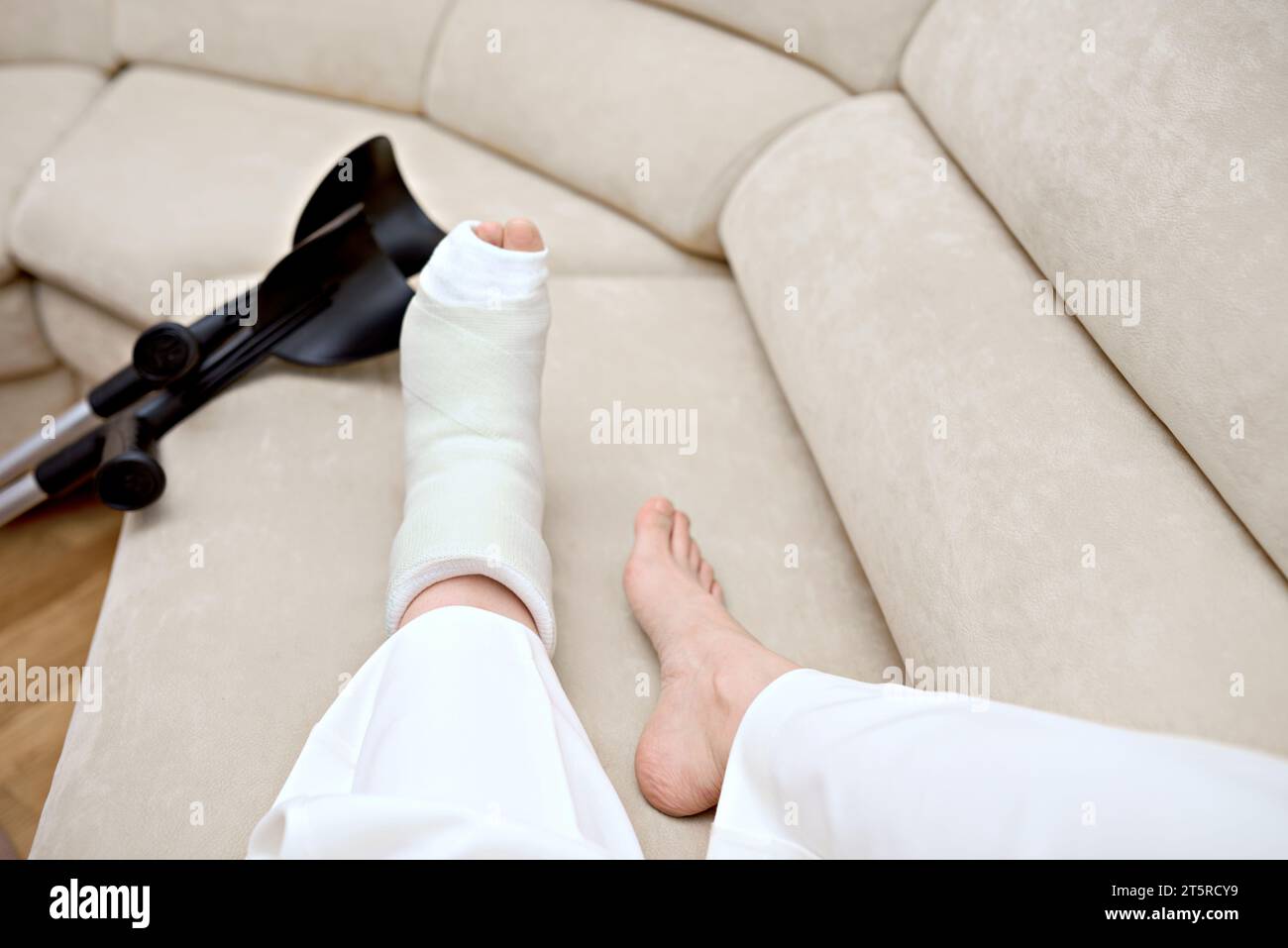 Una giovane donna, con un osso fratturato nel piede, sta riposando sul divano. Tempo di guarigione delle gambe rotto. Riabilitazione dopo un grave incidente fisico Foto Stock