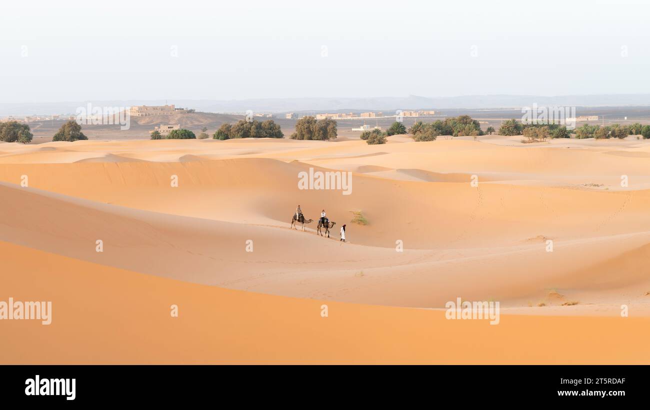 Deserto del Sahara, Marocco - 13 settembre 2022: I turisti in un giro in cammello attraverso le dune di sabbia guidati da un berbero, un classico esempio di turismo nel deserto del Sahara Foto Stock