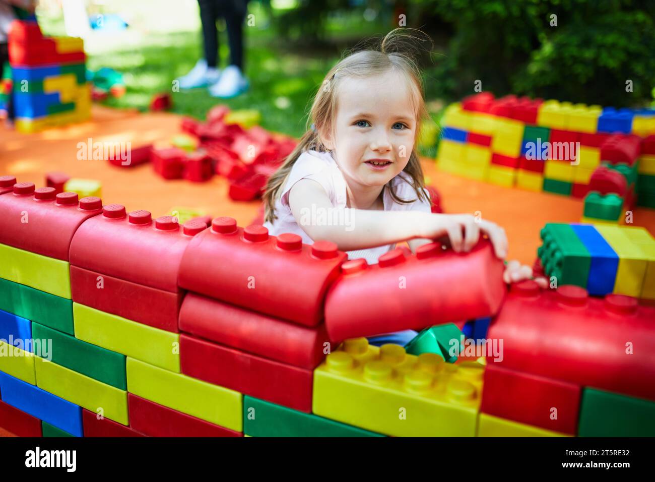 Adorabile bambina in età prescolare che gioca con grandi blocchi di plastica colorata all'aperto, all'asilo o all'asilo. Giochi creativi per bambini Foto Stock