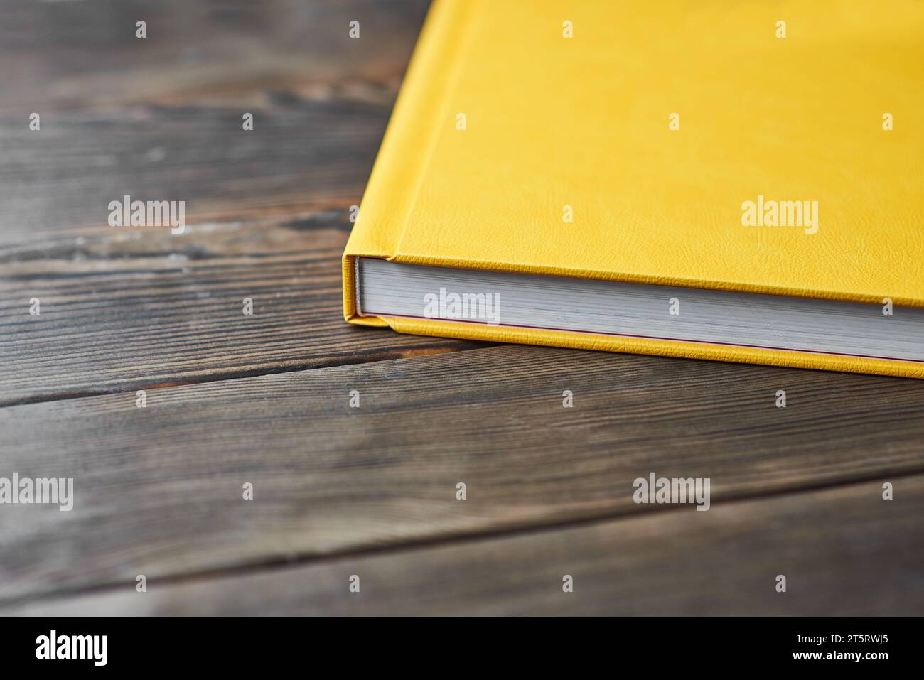 Un'immagine ritagliata di un libro spesso con copertina rigida con texture gialle isolata su un desktop di legno con spazio per la copia del testo. Modello per fotografi o desi Foto Stock