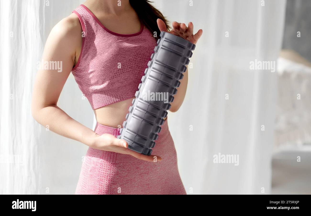 Massaggiatore a rulli in schiuma grigia tenuto da una donna sportiva. Inventario sportivo, strumenti. Massaggio linfatico di drenaggio, rilascio automiofasciale, miglioramento della flessibilità, Foto Stock
