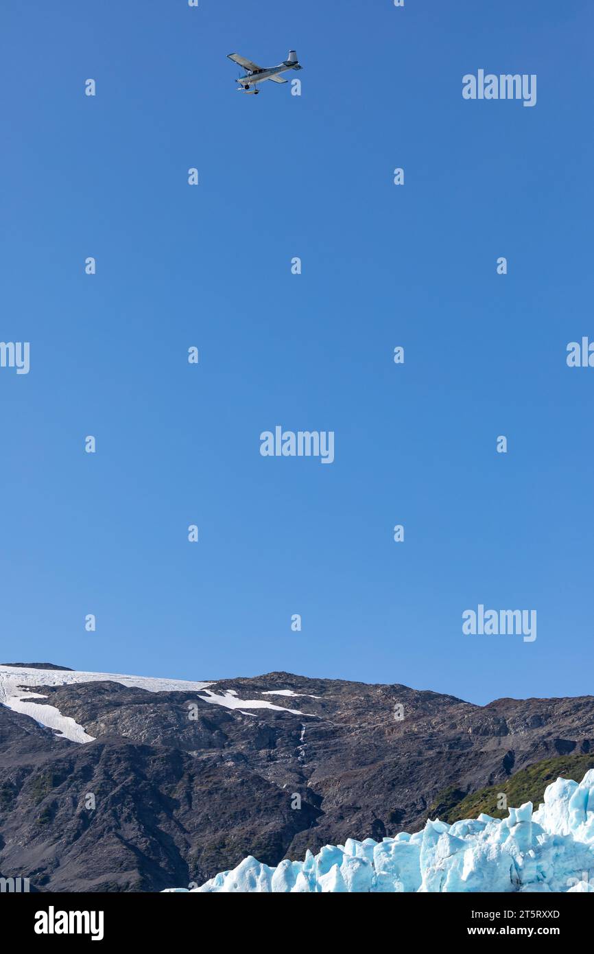 Un piccolo aereo vola sopra un ghiacciaio e una catena montuosa in una giornata limpida. Foto Stock