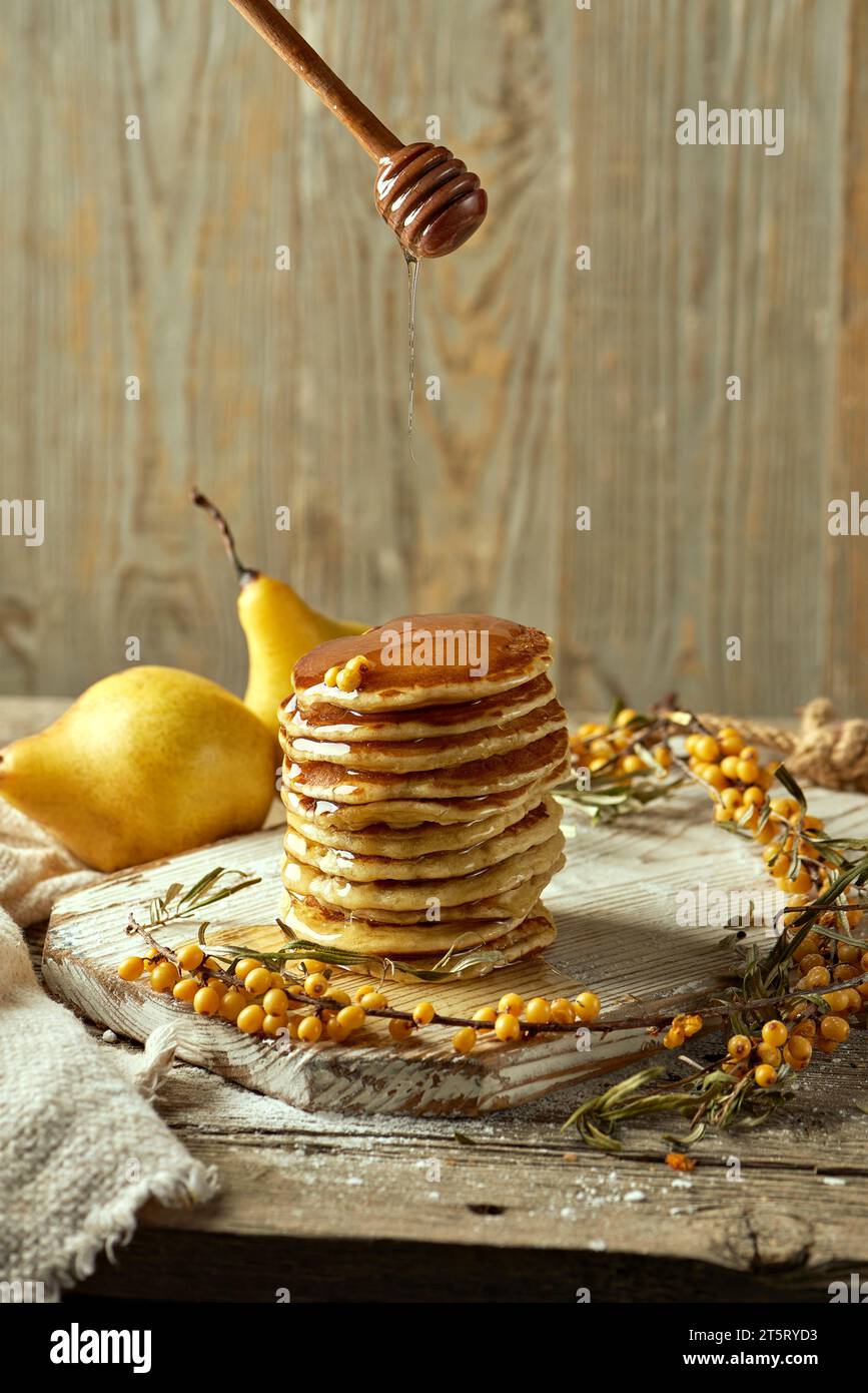 Una tavola di legno con soffici pancake versati con miele, ciuffi di spinopo di mare e due pere. Una componente di festa. Design del menu del ristorante. Cibo Foto Stock