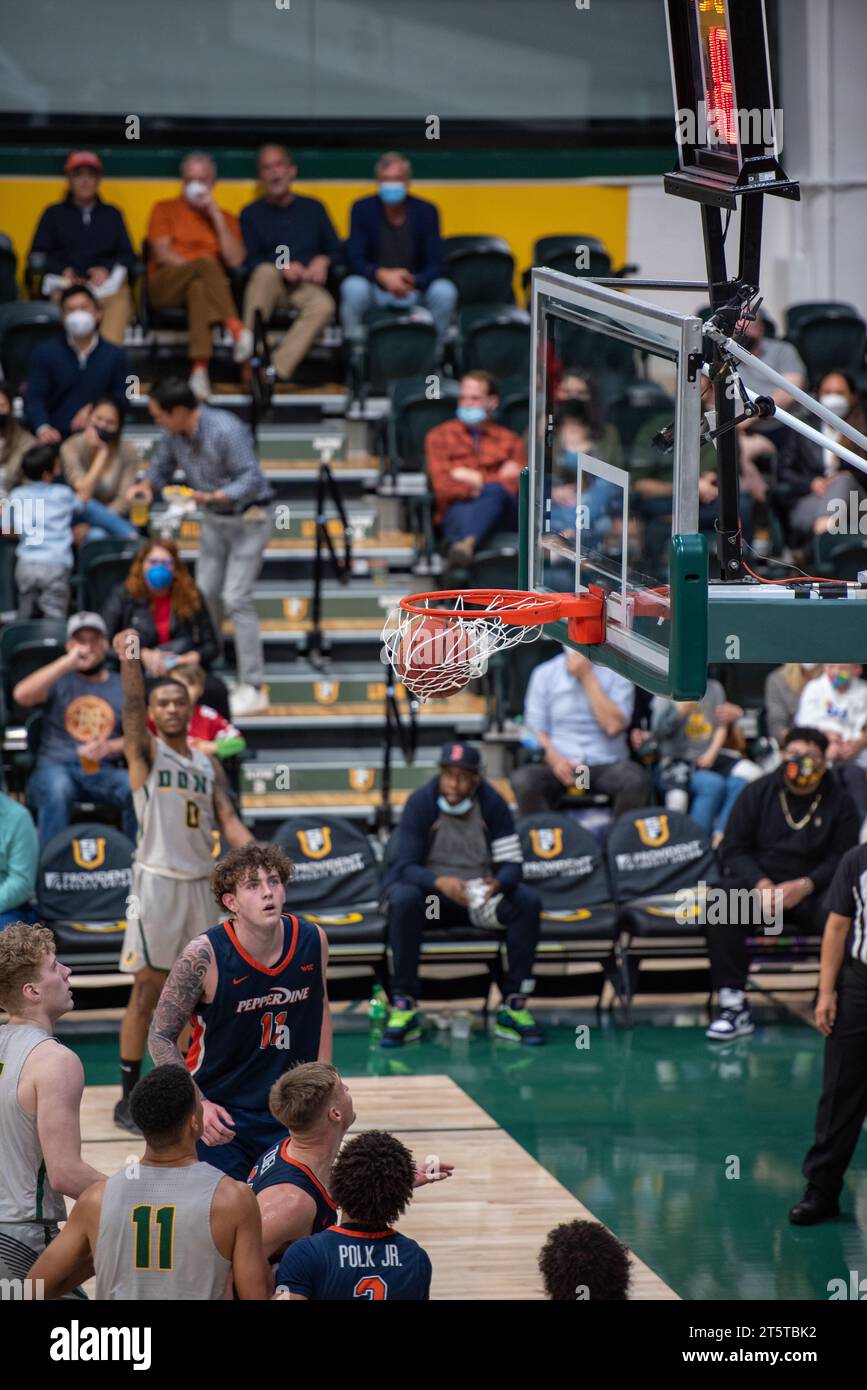 Pallacanestro che sfreccia nel canestro durante l'azione di gioco NCAA college, catturata con dettagli nitidi e una visione chiara dei giocatori e del corvo dell'arena al coperto Foto Stock