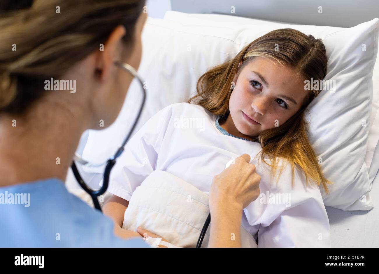 Medico femminile caucasico che utilizza stetoscopio sul torace della ragazza paziente sdraiata nel letto d'ospedale Foto Stock