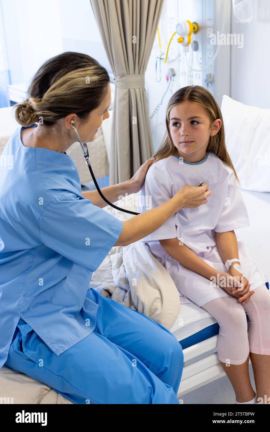 Medico femminile caucasico che utilizza stetoscopio sul torace di paziente ragazza seduto sul letto d'ospedale Foto Stock