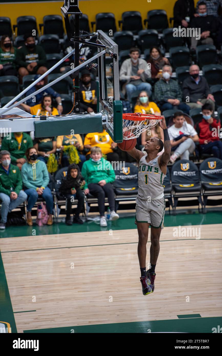 Giocatore di pallacanestro universitario che guida fino al bordo per un layup durante l'azione di gioco NCAA, catturato con dettagli nitidi ed energia dinamica nell'arena indoor. Foto Stock