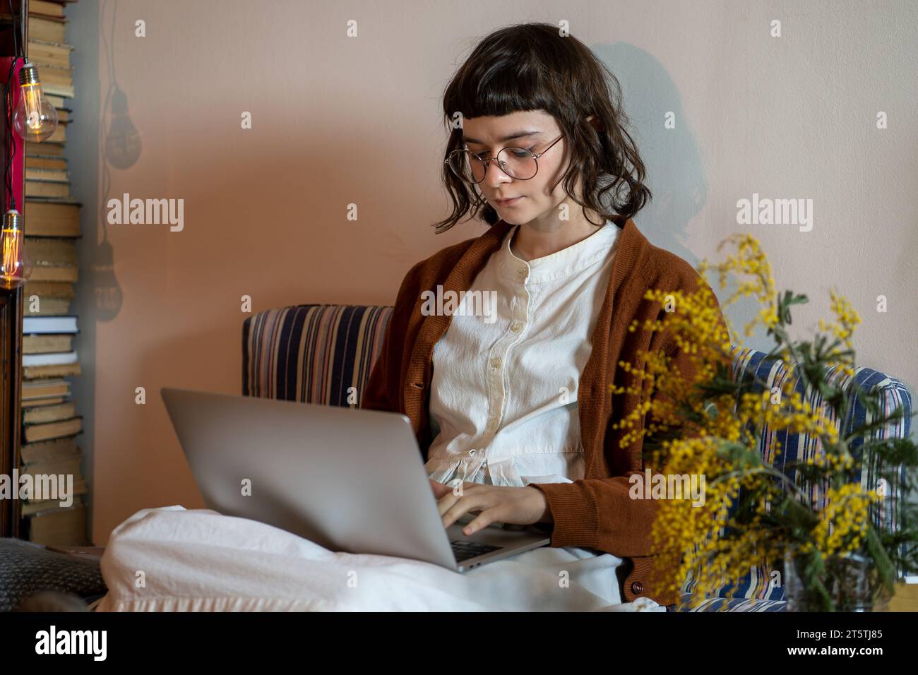 Una ragazza hipster adolescente seduta comodamente sul materasso con un computer portatile che lavora da casa Foto Stock