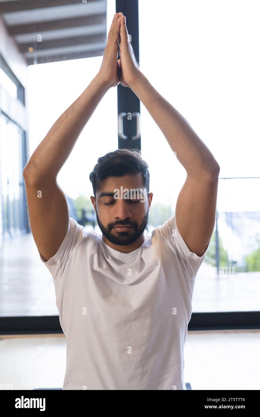Rilassato uomo birazziale seduto, praticando yoga, chiudendo gli occhi e meditando in una stanza soleggiata a casa Foto Stock