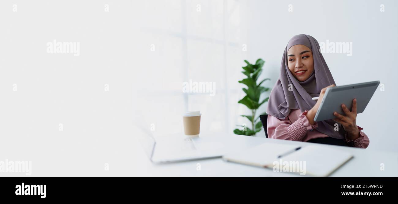 Le donne musulmane usano tablet e laptop per controllare i loro conti al lavoro. Foto Stock