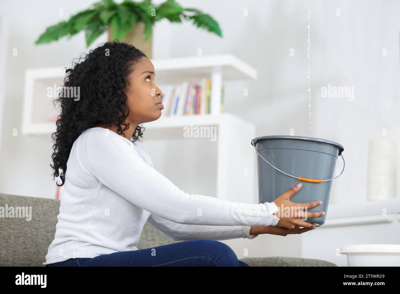 Preoccupato della donna tenendo la benna mentre le goccioline di acqua perdite dal soffitto Foto Stock