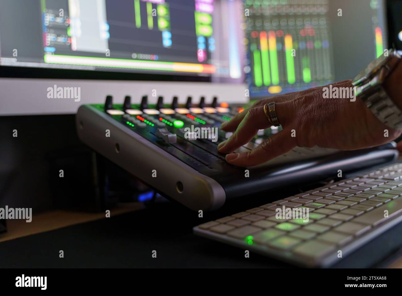 La mano di un tecnico del suono regola i cursori su una console di missaggio audio, mostrando il lato tecnico della produzione musicale e la precisione di missaggio. Foto Stock