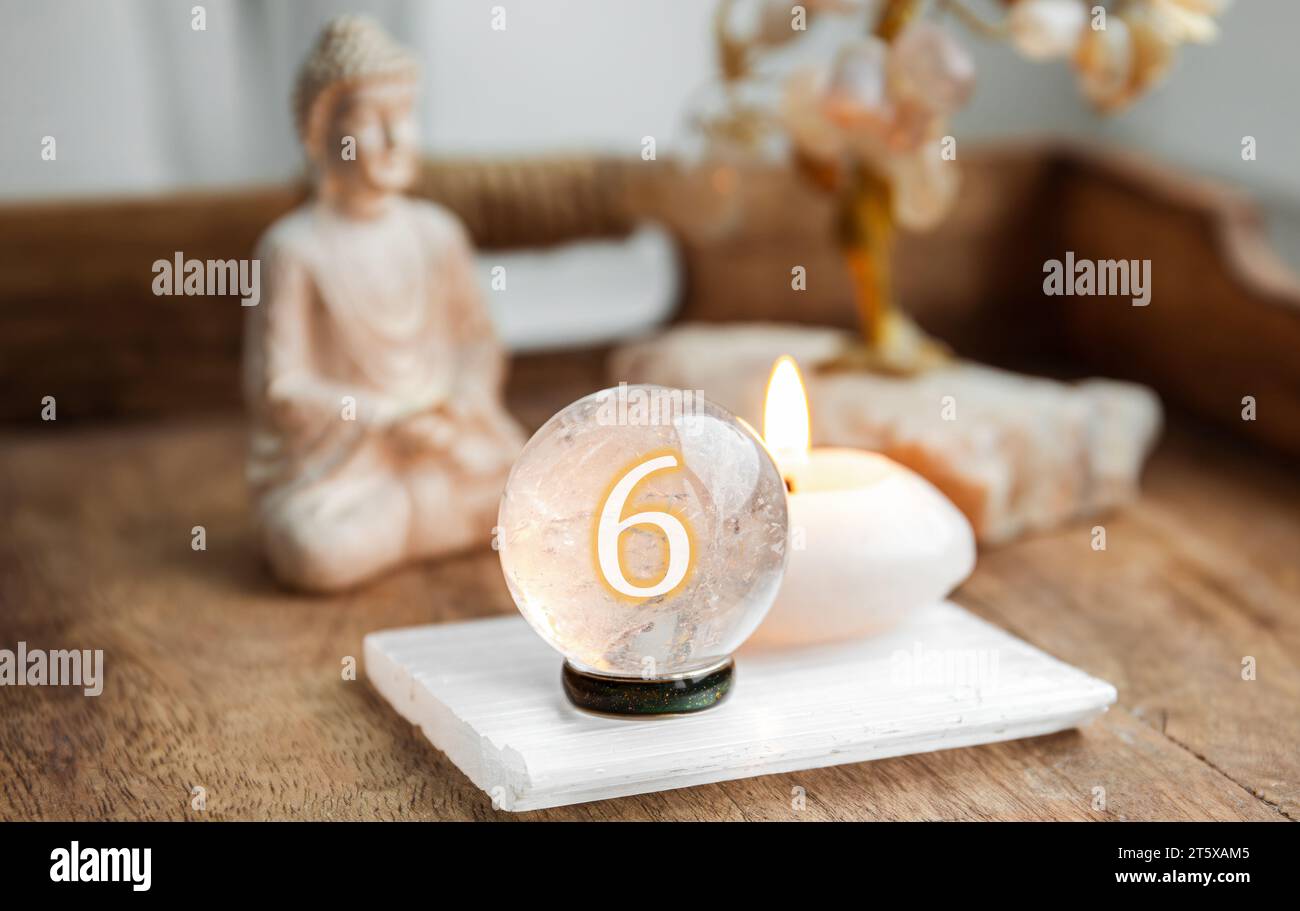 Numero sei sulla sfera Gemstone o sfere di cristallo note come Crystal orbis e orbuculum. Palla di quarzo naturale trasparente su supporto su vassoio di legno in casa. Foto Stock