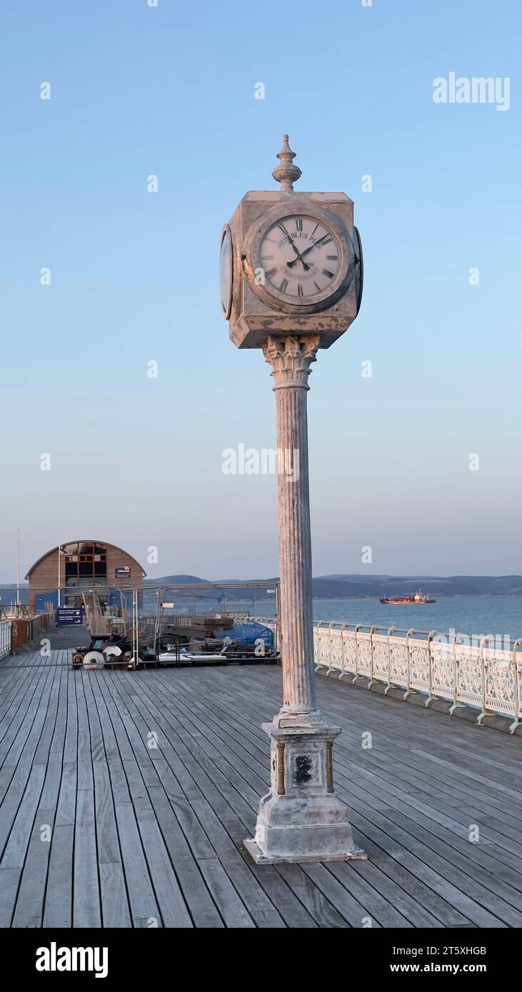 Orologio a torre vecchio stile sul Mumbles Pier con il mare sullo sfondo. Giornata di sole all'inizio del tramonto con cielo color pastello. Foto Stock