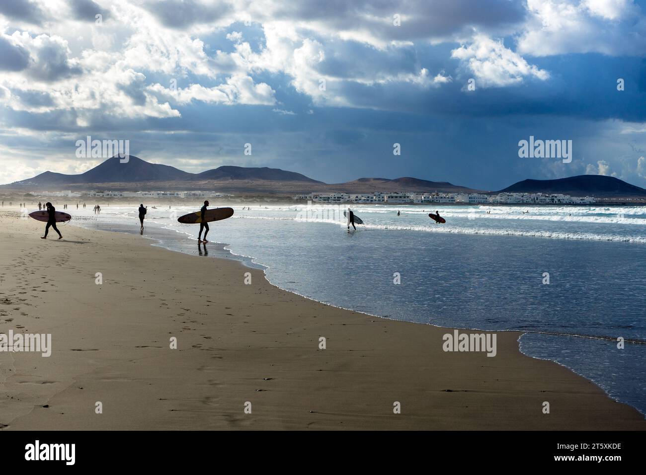 Spagna, Lanzarote, Caleta de Famara: i surfisti entrano ed escono dal mare sulla spiaggia di Famara Foto Stock