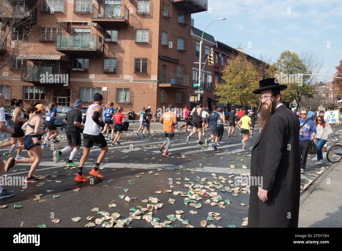 Alla 16 miglia della Maratona di New York, un ebreo ortodosso aspetta uno spazio tra i corridori per attraversare Bedford Ave. A Williamsburg, Brooklyn, New York. Foto Stock