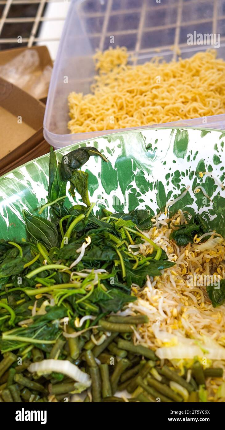 gli spaghetti gialli e le verdure bollite come germogli di soia, spinaci, cavoli, fagioli lunghi, senape bianca verde in un contenitore sono gli ingredienti principali di questo Foto Stock