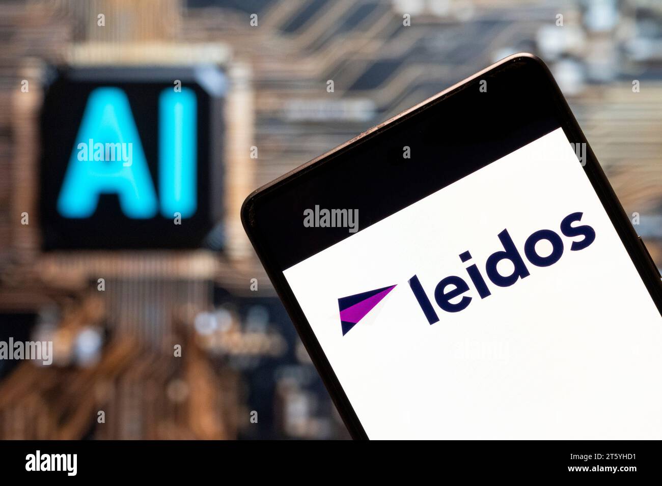In questa immagine fotografica, la società americana di difesa, aviazione, tecnologia dell'informazione e ricerca biomedica precedentemente nota come SAIC, Leidos (NYSE: LDOS), logo visualizzato su uno smartphone con un chip di intelligenza artificiale (ai) e un simbolo sullo sfondo. Foto Stock