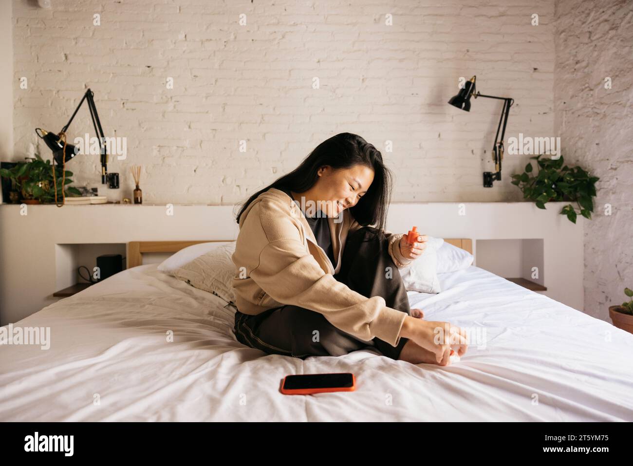 Giovane donna cinese allegra che fa pedicure a letto a casa Foto Stock