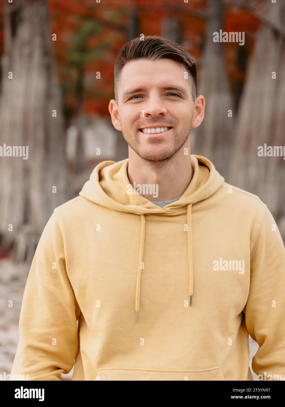 Bell'uomo nella foresta autunnale. Sorridente uomo caucasico con felpa gialla Foto Stock