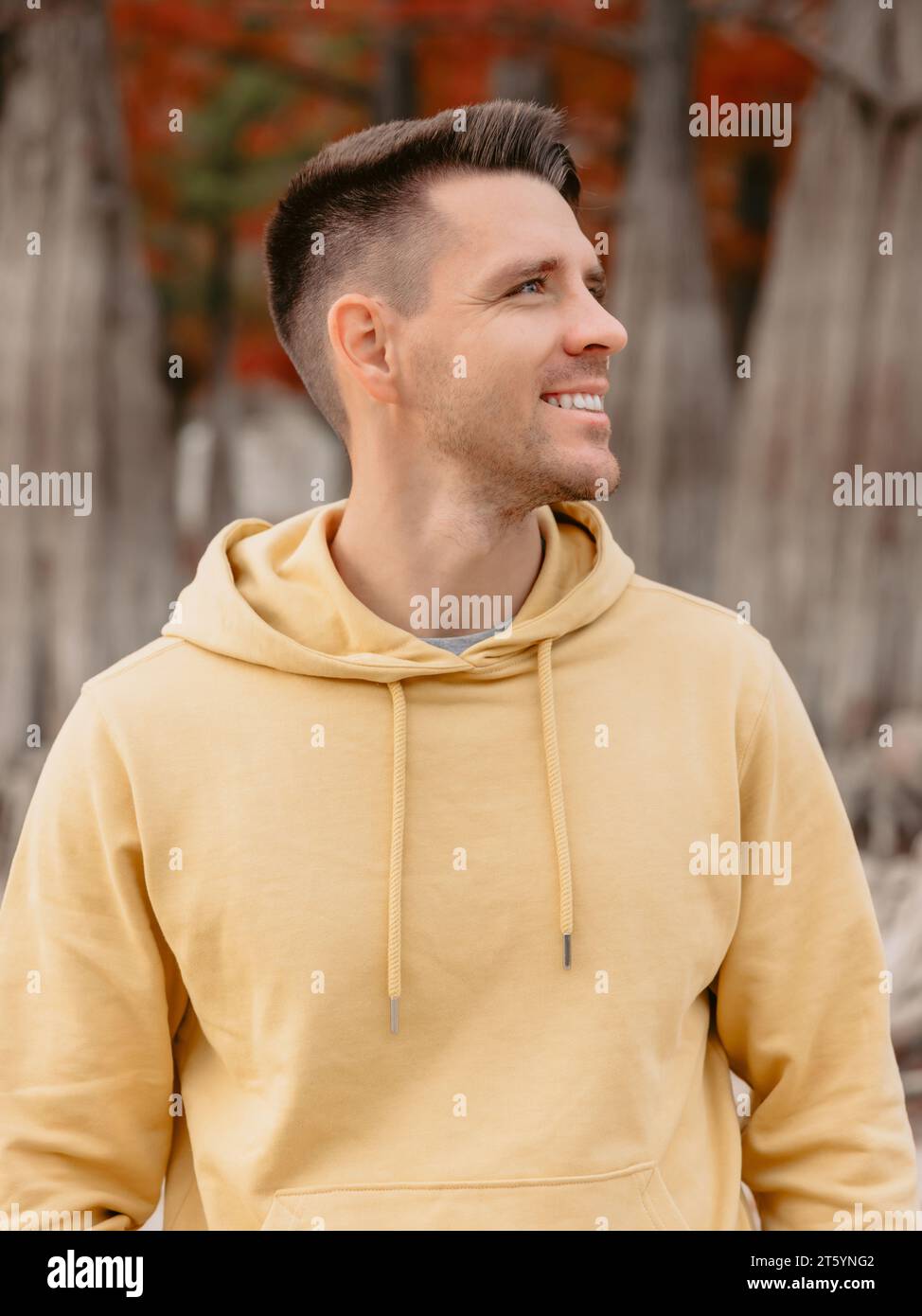 Bell'uomo nella foresta autunnale. Sorridente uomo caucasico con felpa gialla Foto Stock