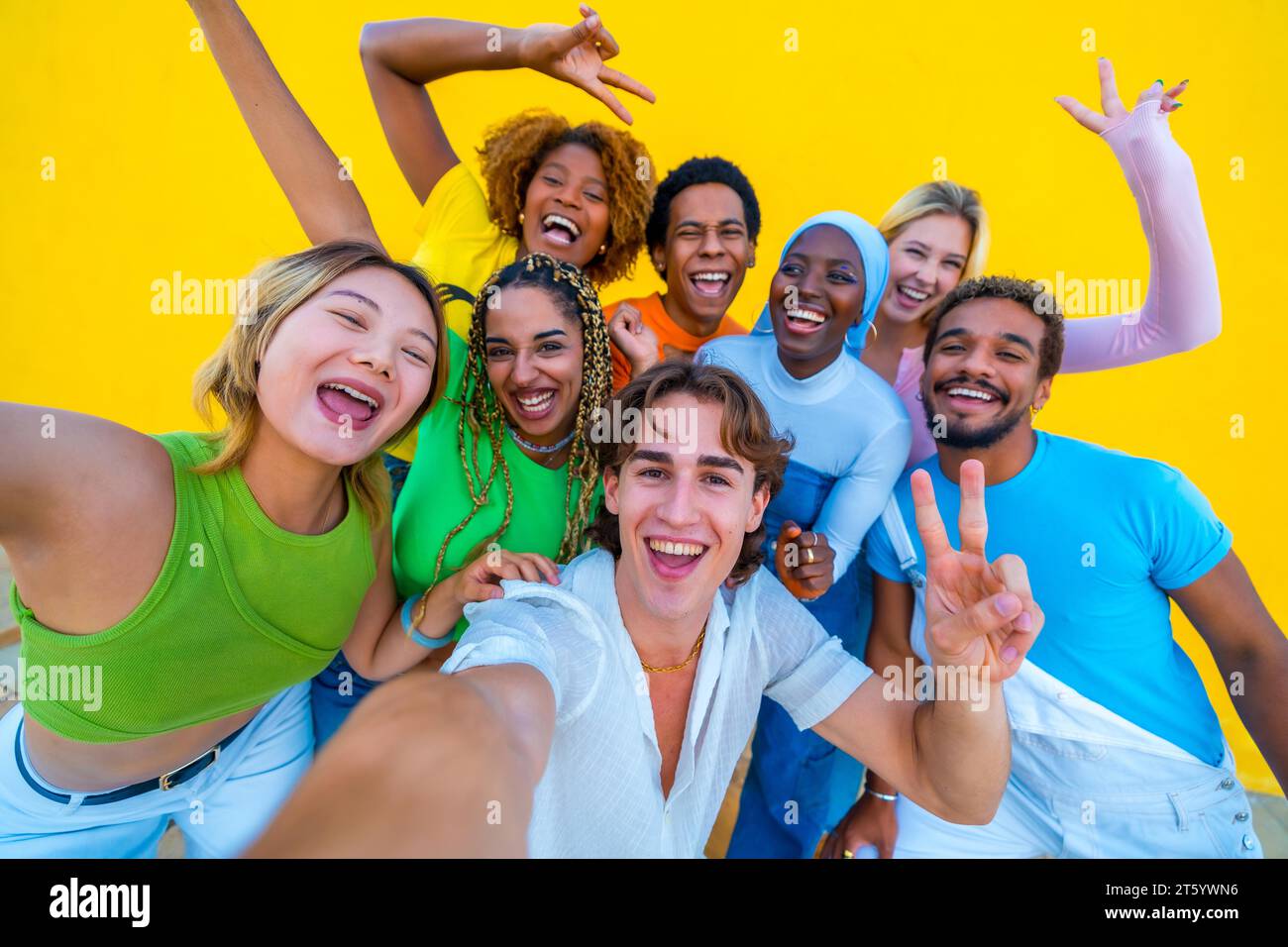 Giovani di diverse etnie che fanno un selfie felice a un raduno accanto a uno sfondo giallo Foto Stock