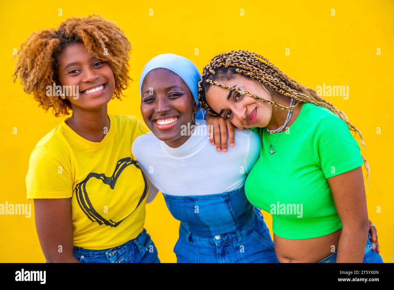 Ritratto ravvicinato di tre donne di diverse etnie sorridenti davanti alla fotocamera su sfondo giallo Foto Stock