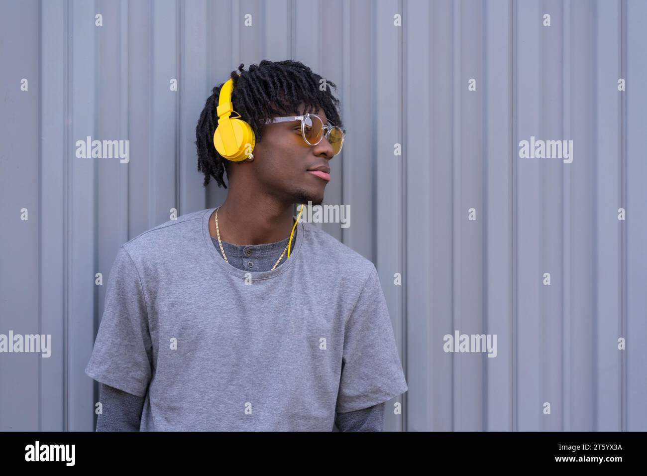 Un giovane africano che ascolta musica addossato a un muro grigio urbano Foto Stock