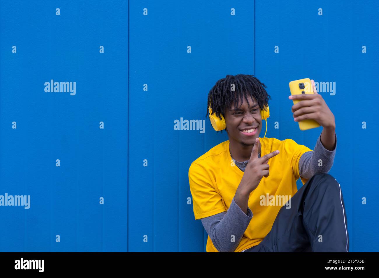 Foto di un giovane afro-americano che ascolta musica e scatta un selfie seduto all'aperto Foto Stock