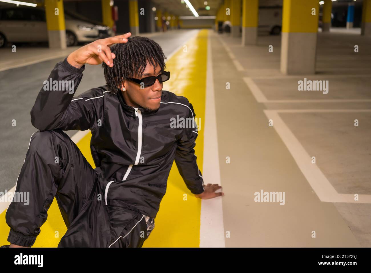 Artista hip hop afroamericano seduto in posa in un garage Foto Stock