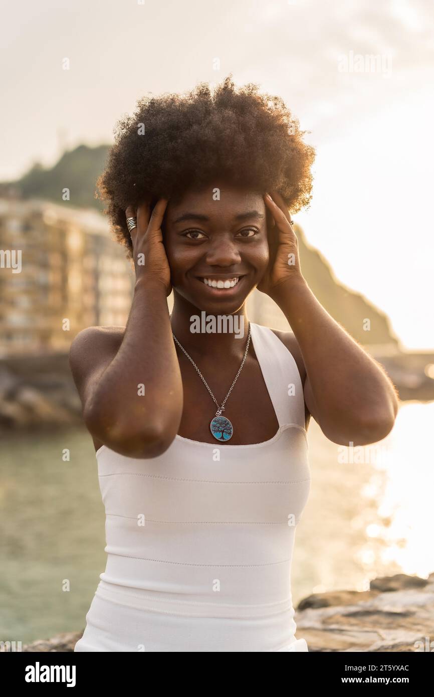 Ritratto verticale di una donna africana felice che posa guardando la macchina fotografica vicino al mare Foto Stock