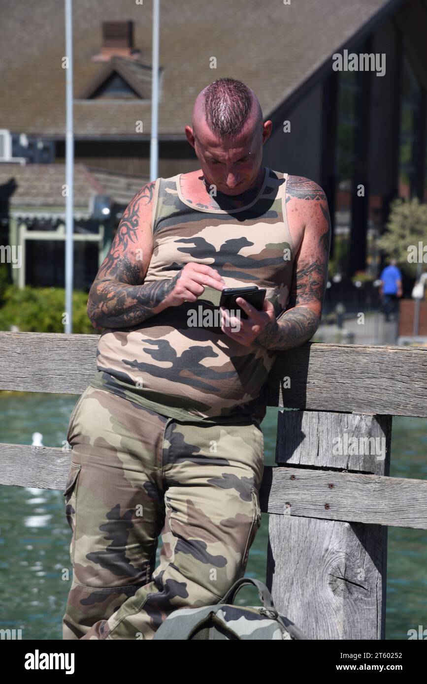 Uomo macho o o uomo tatuato con taglio circolare Crew con abiti camouflage o abbigliamento Camoflaged e telefono di consulenza Foto Stock
