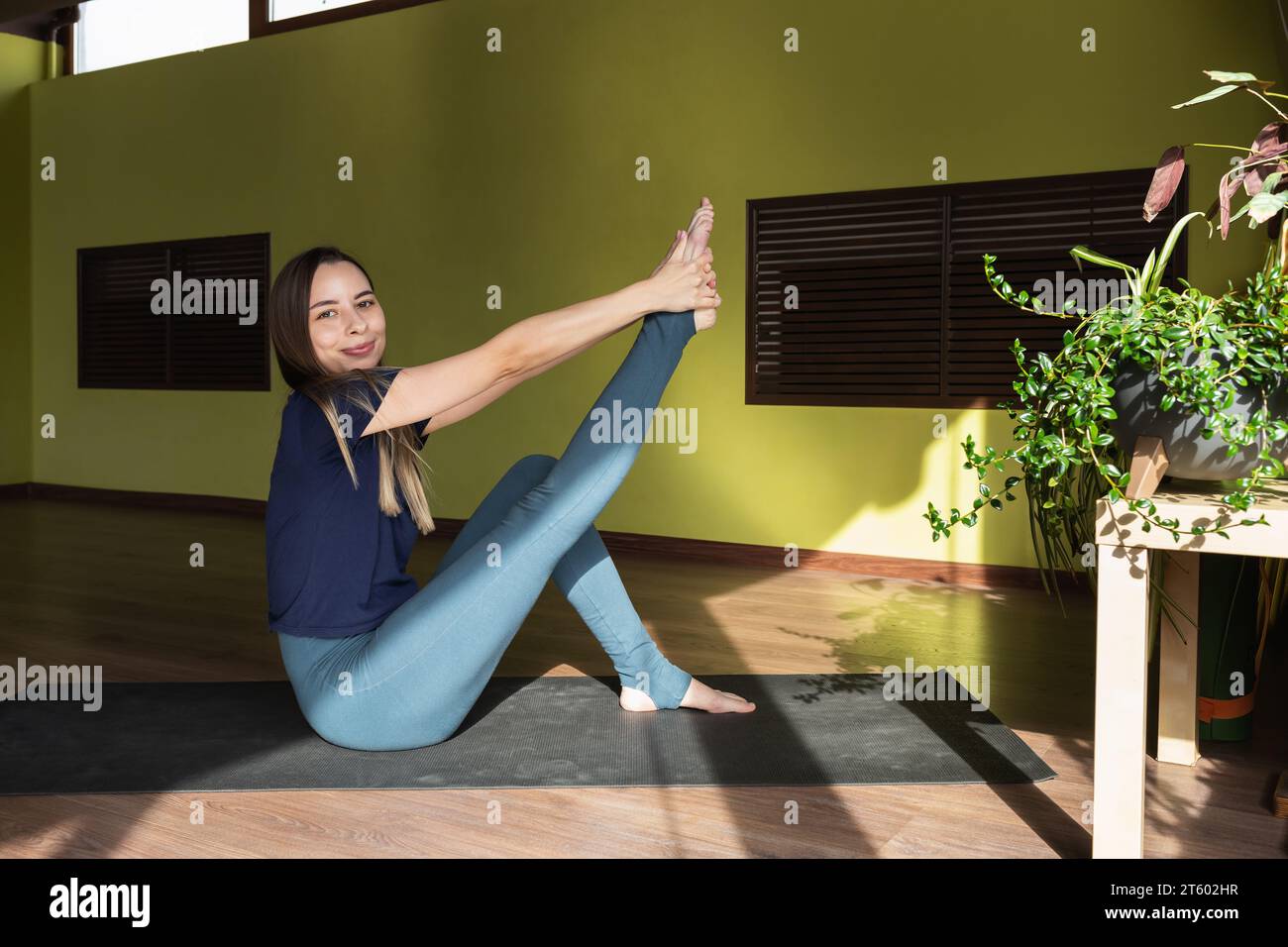 Una giovane donna sportiva sorridente è una donna dai capelli castani che allunga in modo dinamico i muscoli che piegano la gamba al ginocchio, si allena in abbigliamento sportivo Foto Stock