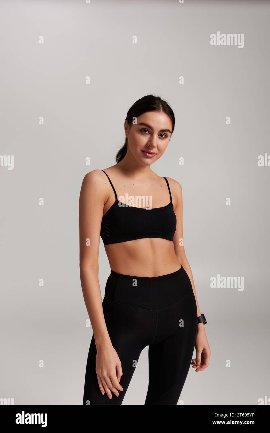 giovane e attraente sportiva con leggings neri e top in rilievo su sfondo grigio Foto Stock