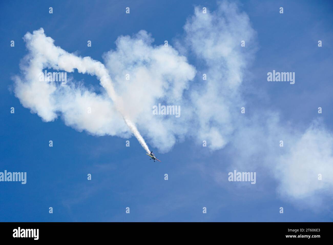Liepaja, Lettonia- 06 agosto 2023: Aereo acrobatico che esegue una manovra acrobatica multipla lasciando una traccia di fumo su sfondo blu Foto Stock