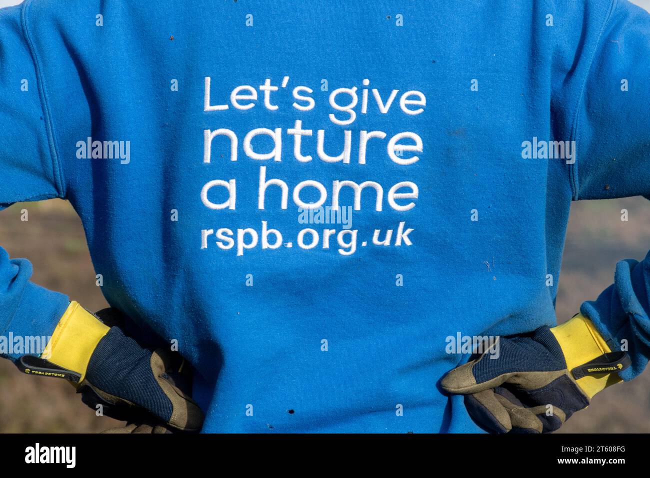 Slogan RSPB, diamo alla natura una casa, su una felpa indossata da un volontario che svolge un lavoro di gestione dell'habitat, Surrey, Inghilterra, Regno Unito Foto Stock