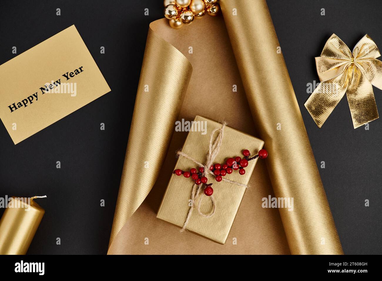 Decorazioni natalizie dorate, biglietti d'auguri per l'anno nuovo vicino alla confezione regalo e carta da imballaggio lucida su nero Foto Stock