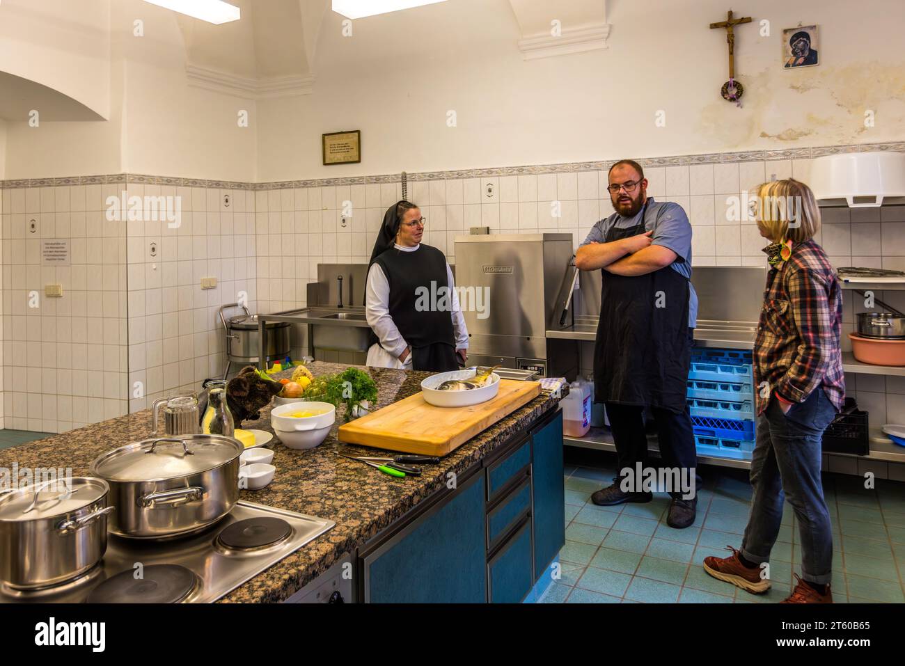 Suora Sophia, direttrice del monastero di Waldsassen, conversa con lo chef Benjamin Standfest e la giornalista Angela Berg nell'antica cucina del monastero della casa ospedaliera San Giuseppe. Verdure e una carpa specchio per la preparazione del "Karpfen blau" (carpa blu) sono già pronti sul bancone. Waldsassen, Baviera, Germania. Foto Stock