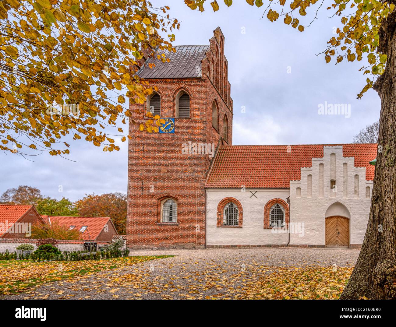 Passeggiata della chiesa con foglie cadute che conducono a una chiesa rurale con una torre in mattoni a Helsinge, Danimarca, 7 novembre 2023 Foto Stock