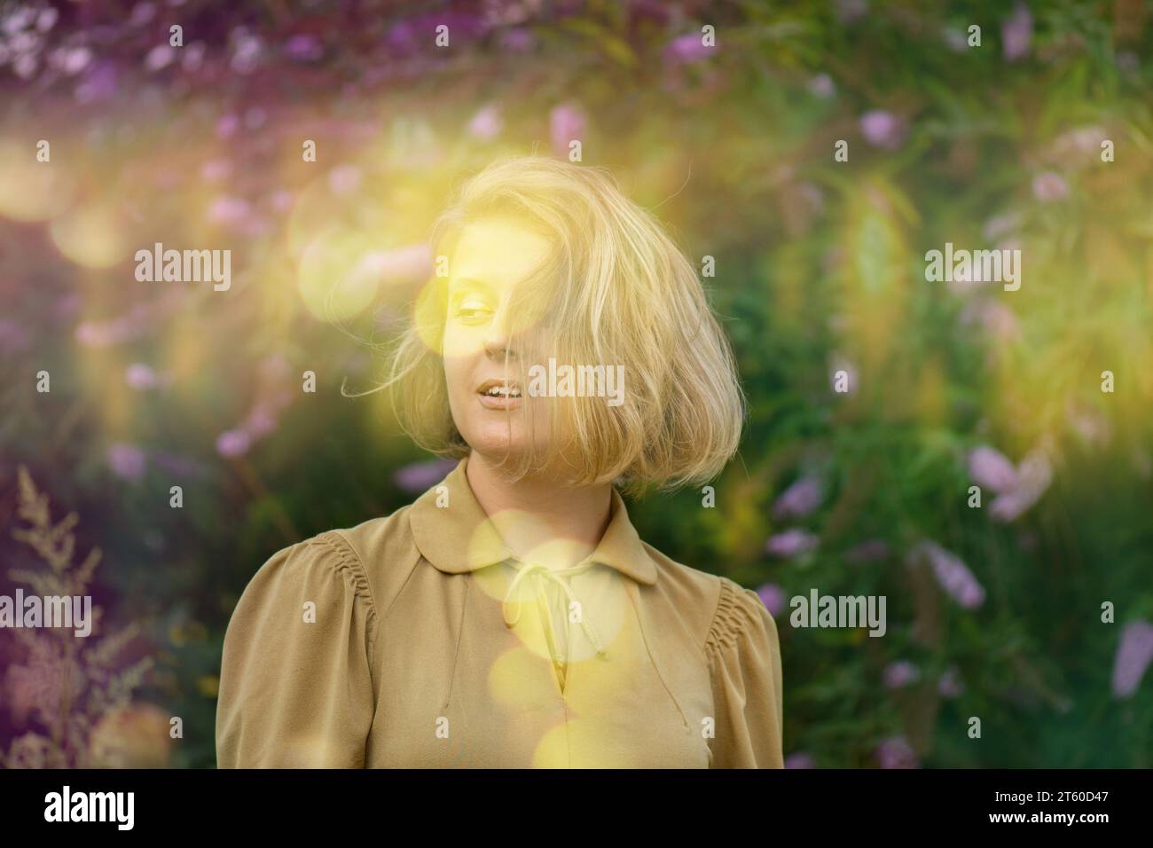 Concetto Lifestyle Happy Emotions. Giovane donna felice e felice con un sorriso che guarda felicemente in camera. Donna vicino ai fiori della buddleia Foto Stock