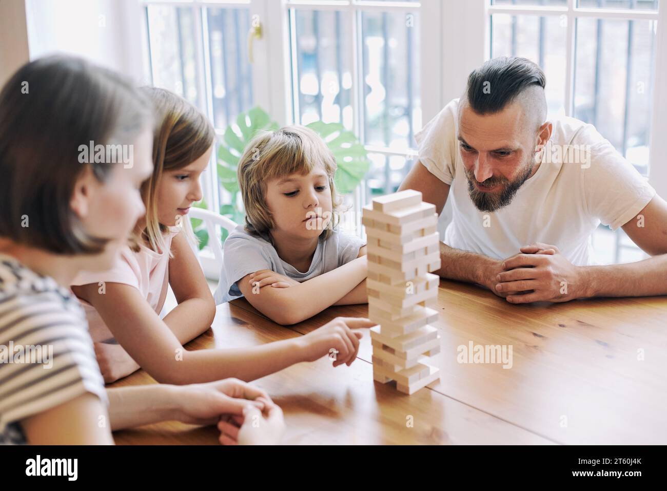 Gli amanti dei giovani genitori con figli piccoli e figli si divertono a divertirsi, giocando a un gioco di rimozione dei blocchi seduti al tavolo nel soggiorno durante il weekend Foto Stock