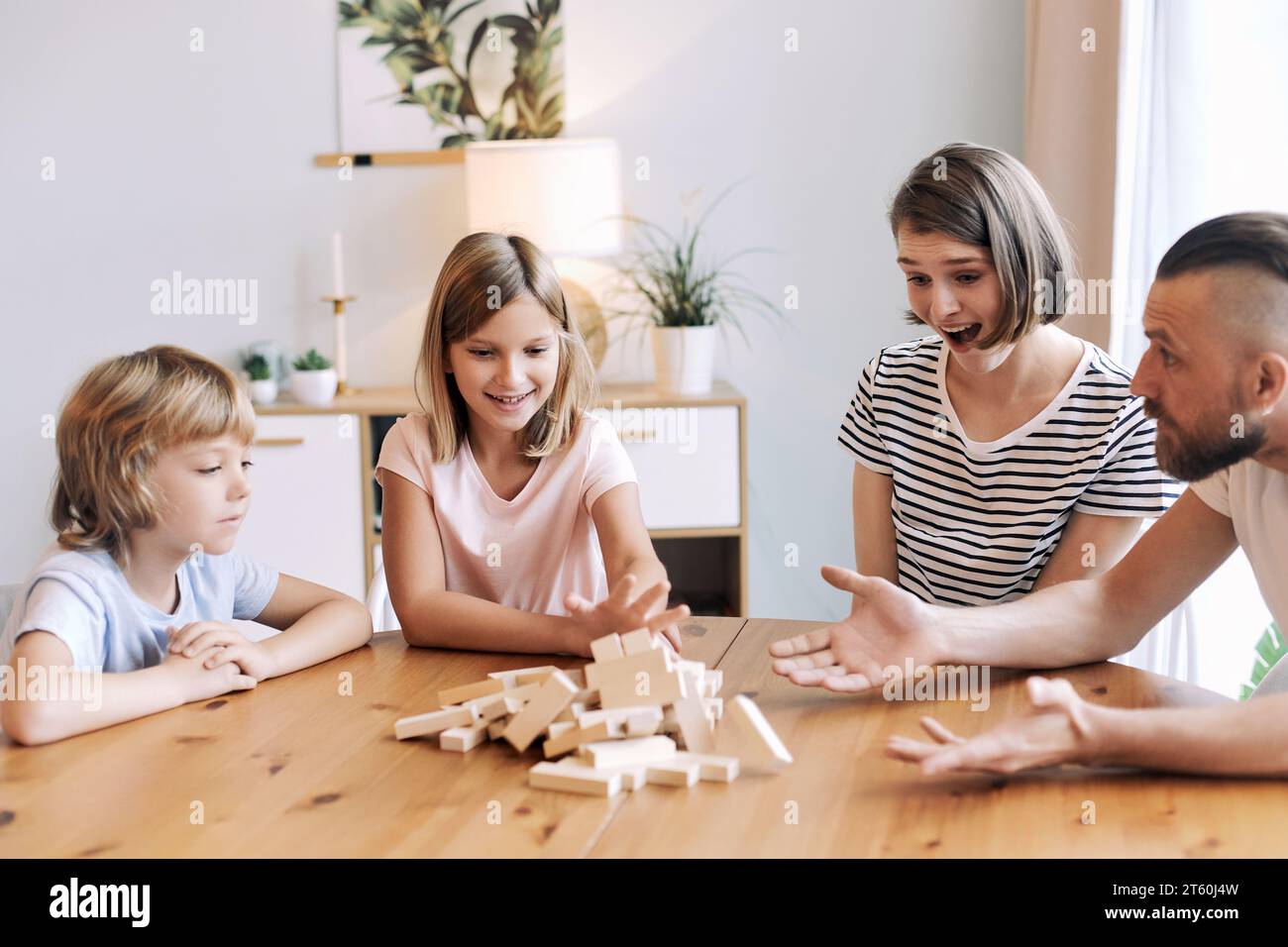 Gli amanti dei giovani genitori con figli piccoli e figli si divertono a divertirsi, giocando a un gioco di rimozione dei blocchi seduti al tavolo nel soggiorno durante il weekend Foto Stock