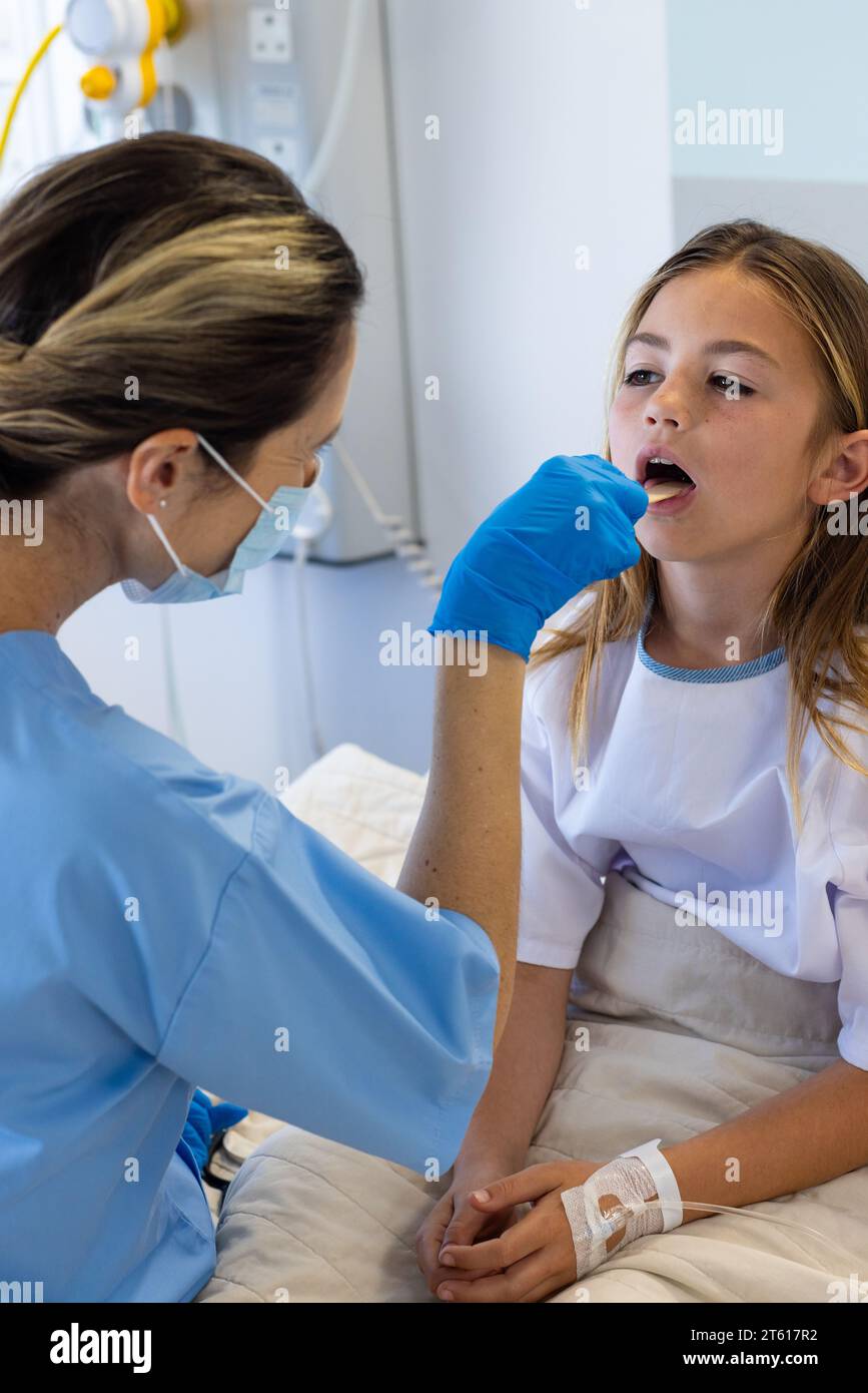 Medico femminile caucasico in maschera e guanti utilizzando spatola controllo gola di ragazza paziente in ospedale Foto Stock