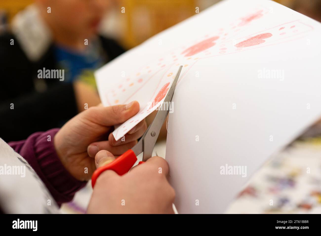 Primo piano delle mani del bambino che taglia un pezzo di carta con le forbici Foto Stock